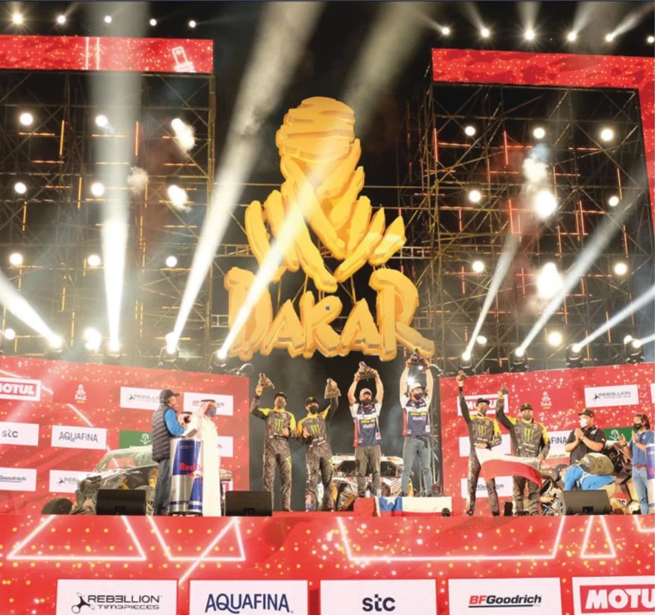 Dakar Rally stage with trophy sculpture, red screens and live lighting